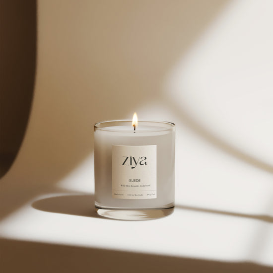 Burning Ziya candle in a glass jar set infront of a moody neutral background.